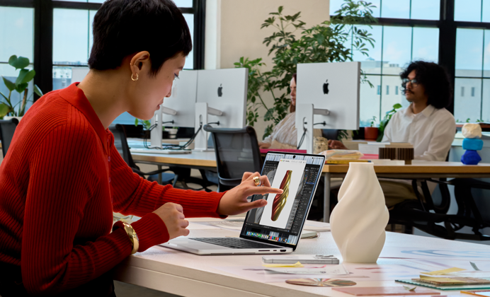 Una persona in un ufficio open space usa il Touch per interagire con un MacBook Pro con display PROLED XDR
