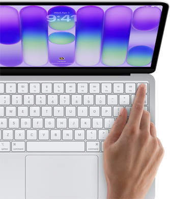 MacBook Neo color argento che mostra la schermata di login, con il dito di una persona appoggiato sul sensore Touch ID nell’angolo in alto a destra della tastiera
